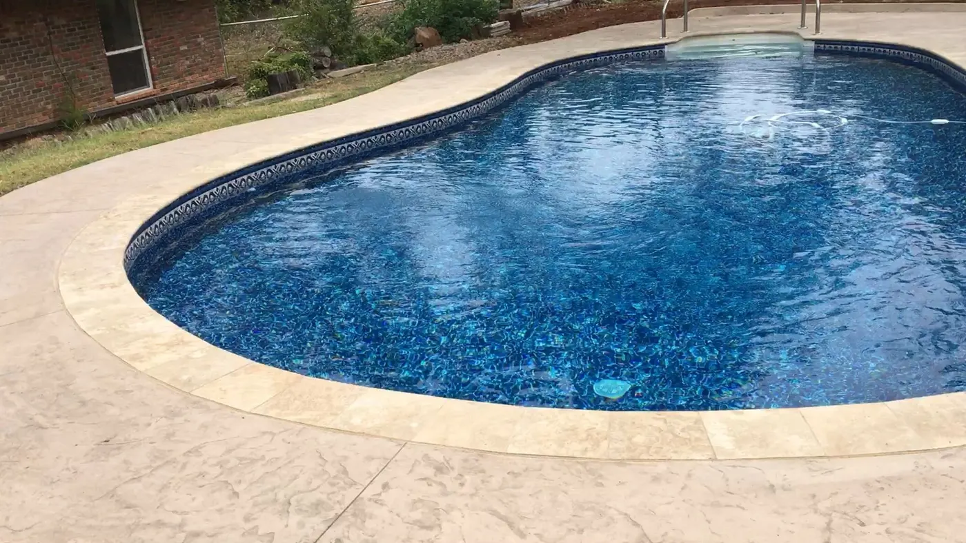 Same pool finished with a new liner, travertine coping, and a stamped concrete deck