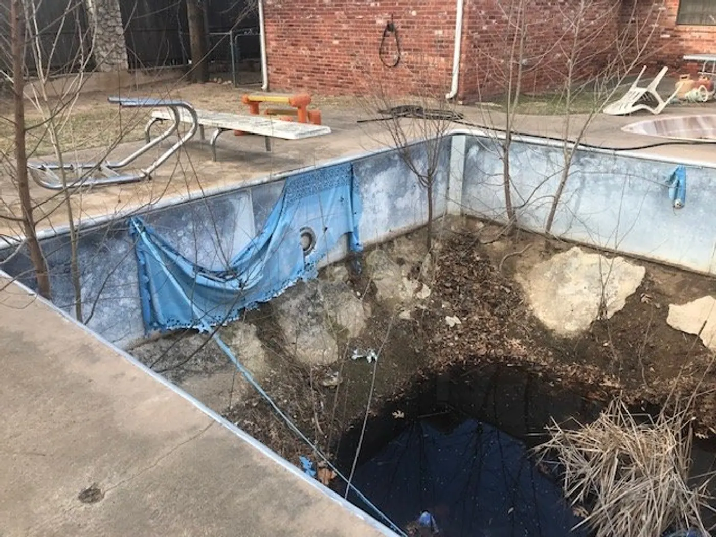 Drained rectangular pool with collapsed old vinyl liner and debris before renovation