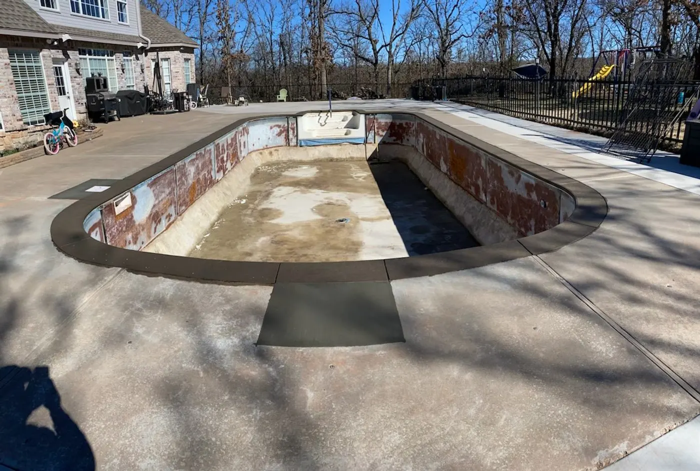 Drained pool with the old liner stripped down to rusted walls before renovation