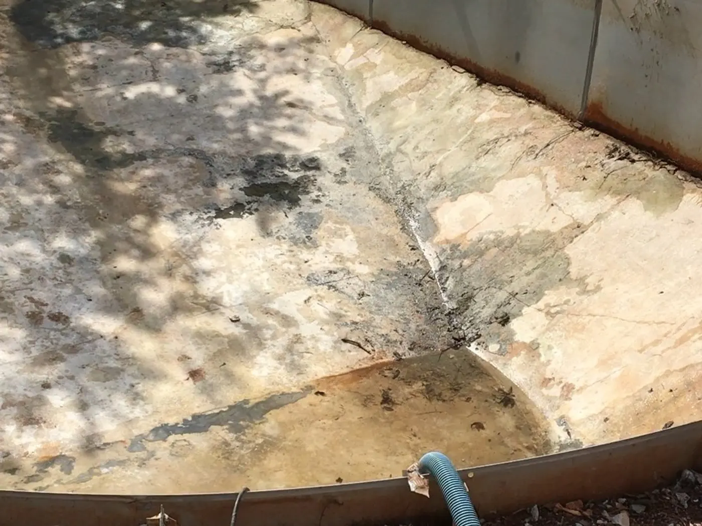 Empty vinyl pool with the old liner removed and bare dirt around it before renovation