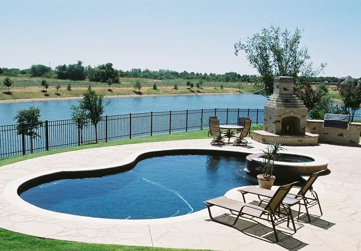 Kidney-shaped concrete pool with fireplace, water feature, and scenic lakeside views
