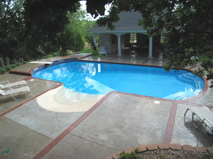 Blue pool with attached spa featuring stone waterfall and columned pavilion