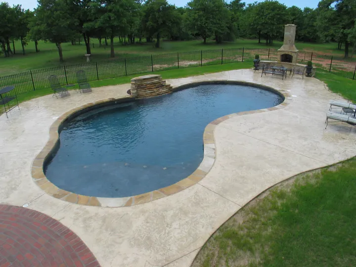 Large kidney-shaped concrete pool in natural wooded setting with simple design