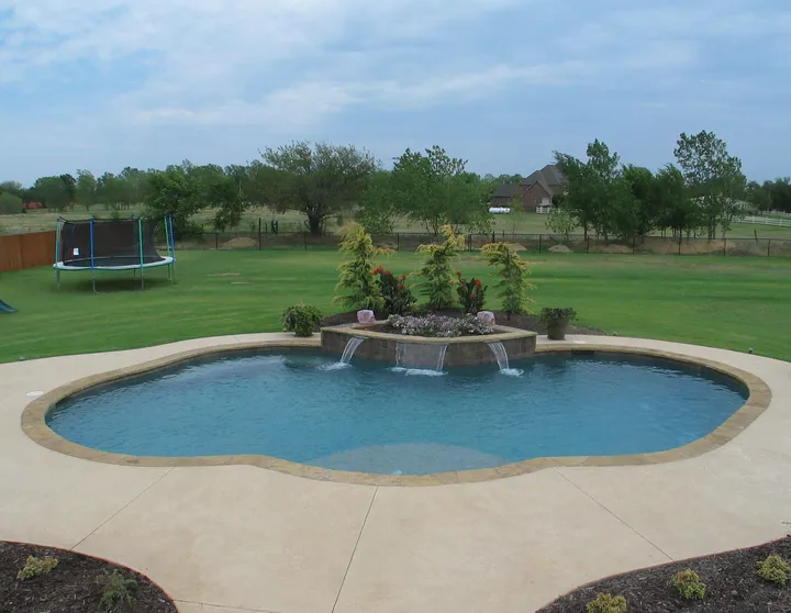 Simple oval concrete pool with central waterfall island feature in open yard