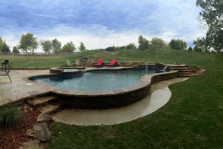 Curved freeform pool with natural stone edging and landscape setting with red lounge chairs