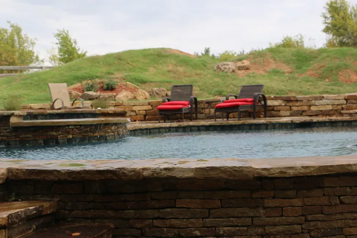 Landscape view of curved freeform pool with stone walls and concrete decking in natural setting