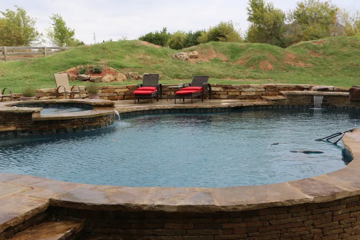 Curved main pool with attached smaller spa/hot tub feature and landscaping