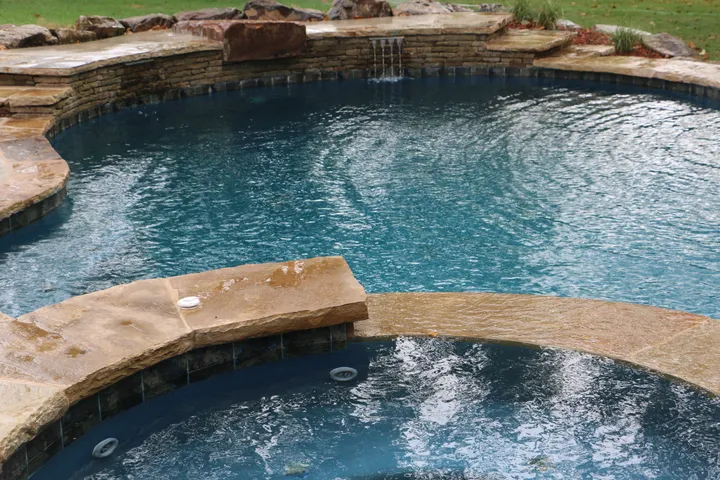 Main pool and spa configuration with stone walls, concrete decking, and seating area