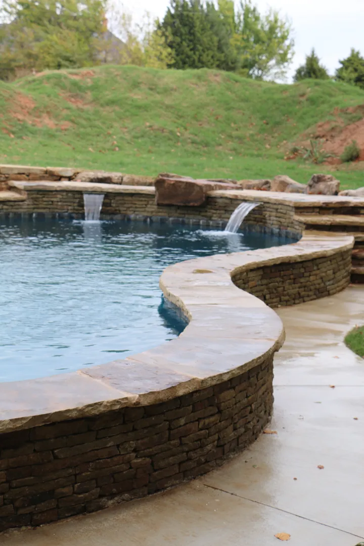 Wide landscape view of complete pool installation with stone walls and natural surroundings