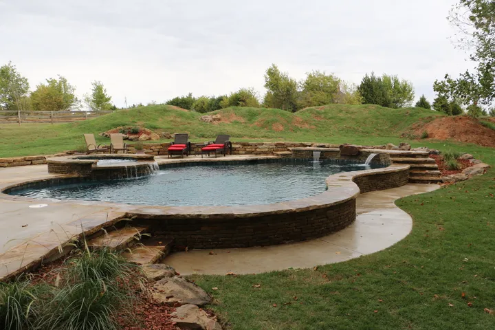 Curved pool with integrated stone walls and concrete decking in afternoon lighting