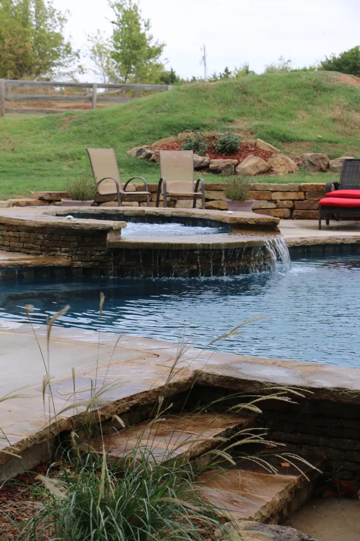 Landscape overview of complete freeform pool with dual spa features and stone accents