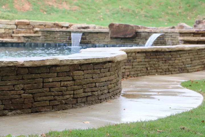 Curved stone pool with dual waterfall features and concrete decking