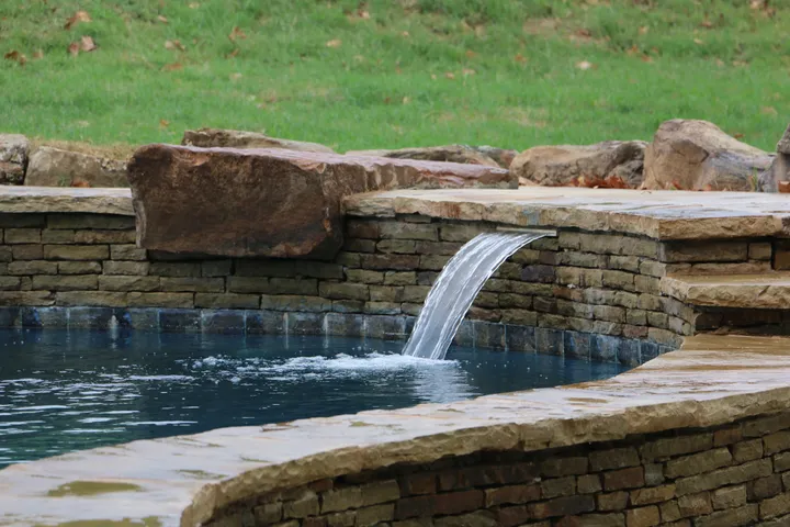 Stone-lined pool featuring cascading waterfall with natural rock accents