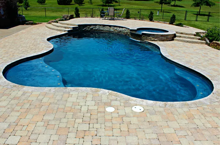 Large curved pool with integrated spa and paver deck in open setting