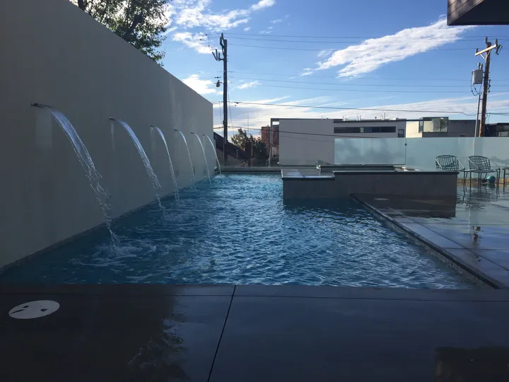 Modern pool with wall-mounted water spouts creating arc fountains into pool