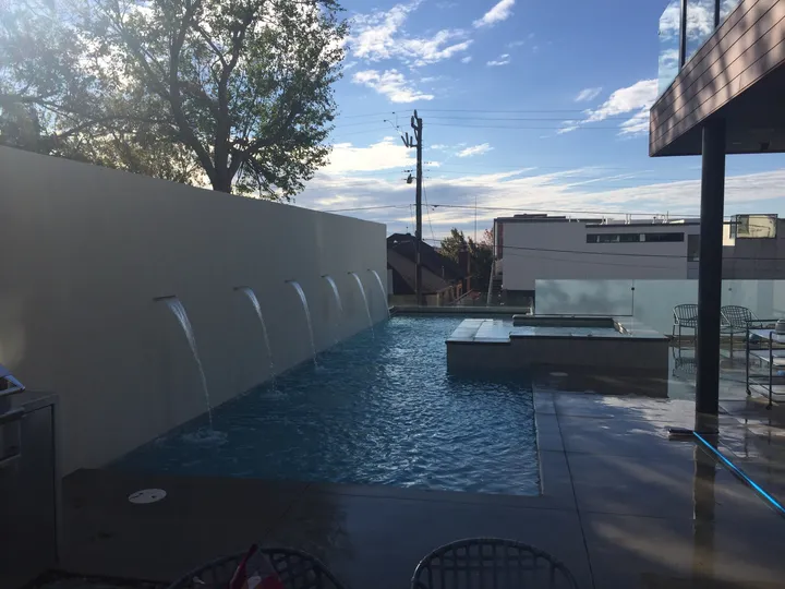 Wider angle of modern pool showing multiple wall fountains and spa with outdoor seating
