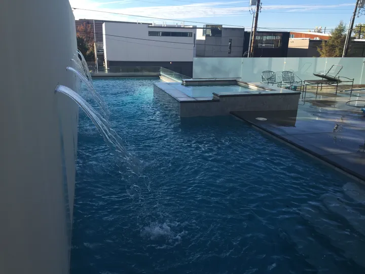 Close-up of wall fountain arcs flowing into modern pool with spa visible