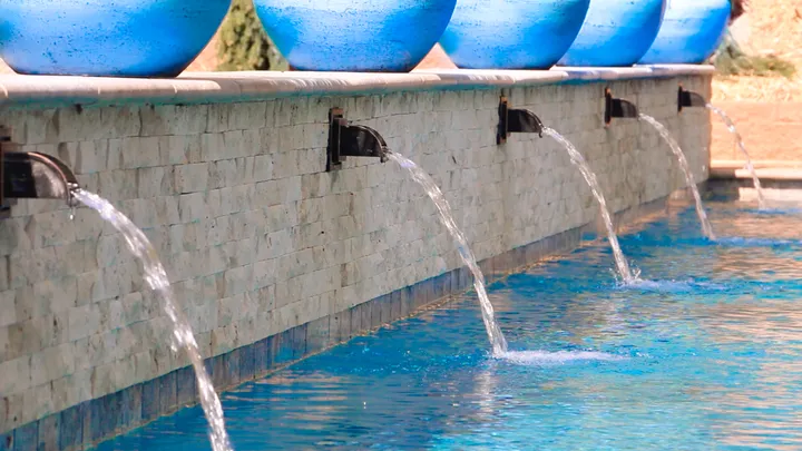 Sleek rectangular pool with concrete decking, metal railing, and natural landscape background