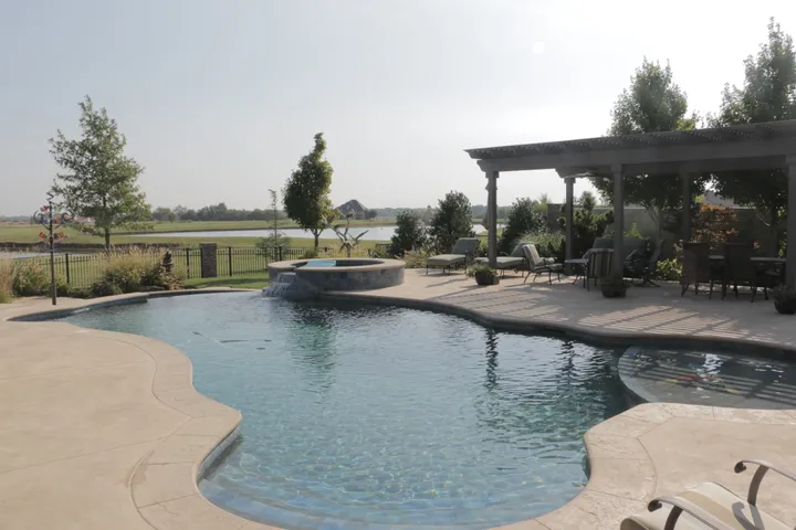Curved freeform pool with attached spa and shade structure in rural setting