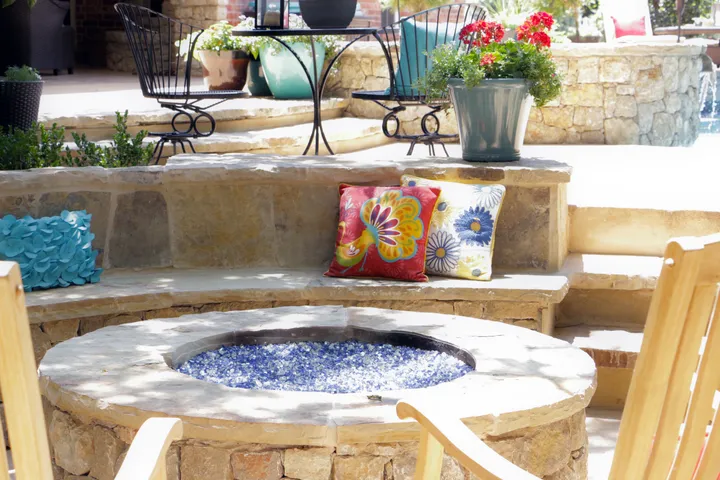 Circular fire pit with blue fire glass and built-in stone seating with patio furniture