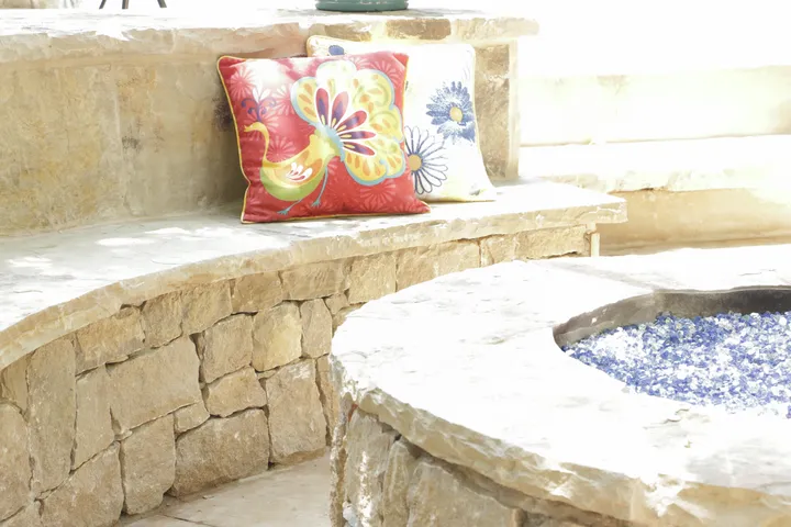 Close-up of stone fire pit edge with colorful pillows and stone surround