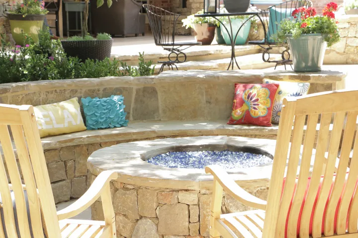 Circular fire pit with blue fire glass surrounded by bench seating and decorative pillows