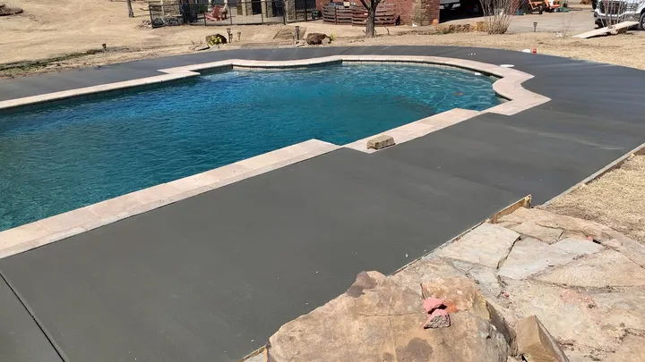 New gray concrete deck with travertine coping around a pool and spa