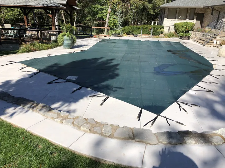 Green mesh safety cover on a rectangular pool with a stone-edged deck