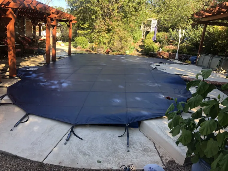 Navy safety cover on a freeform pool beside a cedar pergola