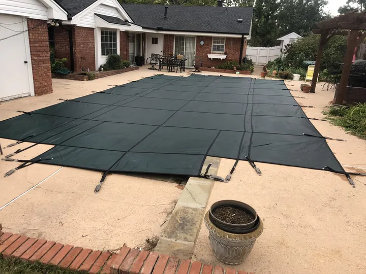 Green safety cover on a rectangular pool behind a brick home