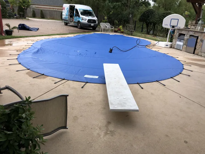 Blue safety cover on a round pool with a diving board