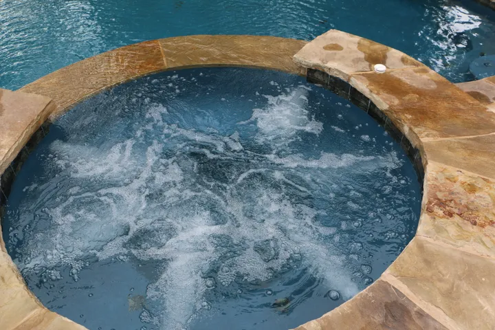 Circular hot tub with jets active, showing water circulation and stone edging