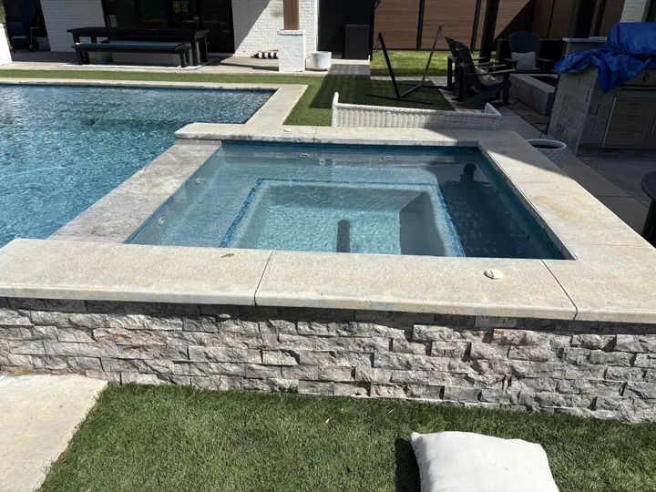 Stacked-stone raised spa beside a rectangular pool at a modern home