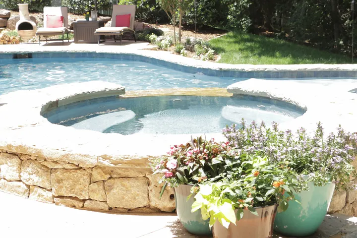 Spa with stone surround and colorful planters, part of large backyard pool complex