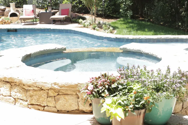 Spa with stone surround and colorful planters in backyard pool complex