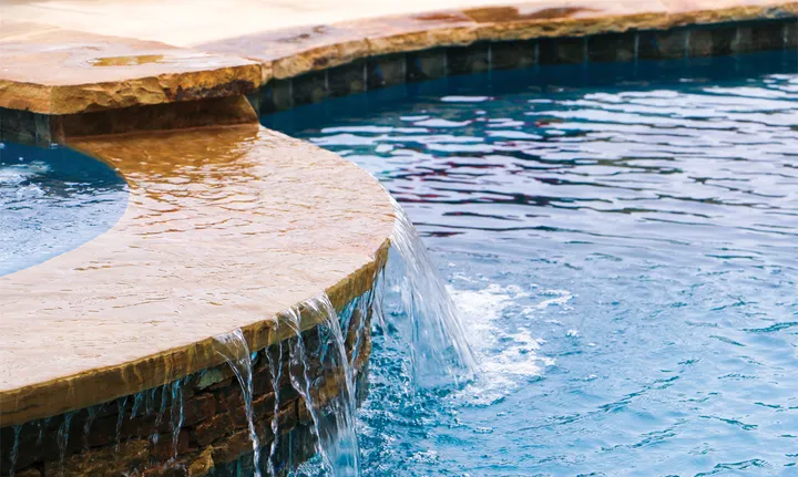 Natural stone waterfall feature with flowing water cascading into elegant pool