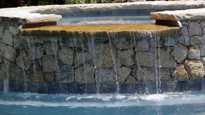 Stone waterfall feature with multiple cascades flowing into pool with dramatic lighting