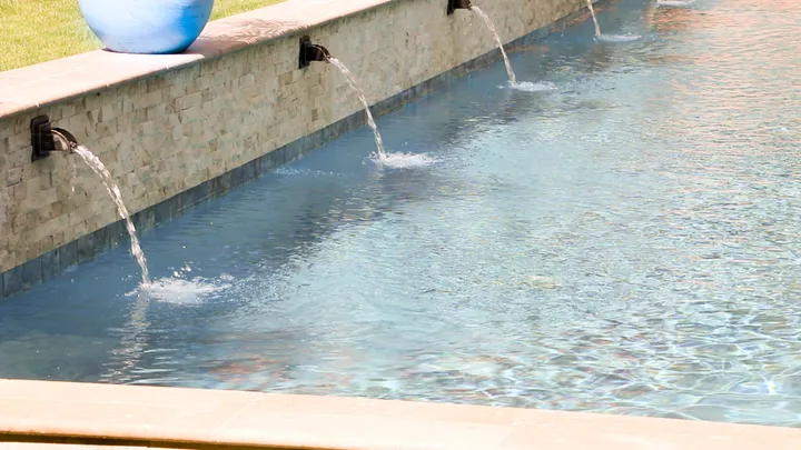 Multiple water jets creating wall of cascading water along pool wall with planter