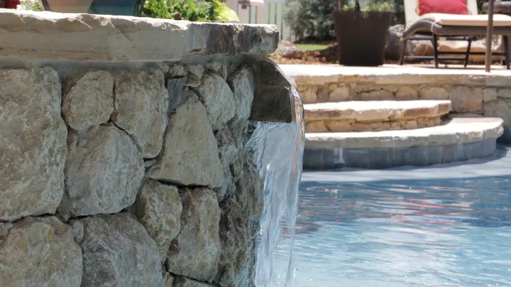 Stone waterfall feature flowing into luxury pool with stone coping