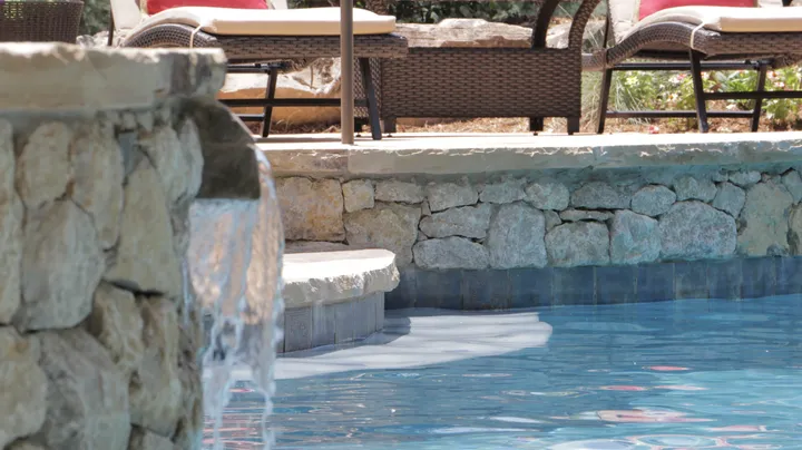 Stone waterfall cascading into resort-style pool with lounging area