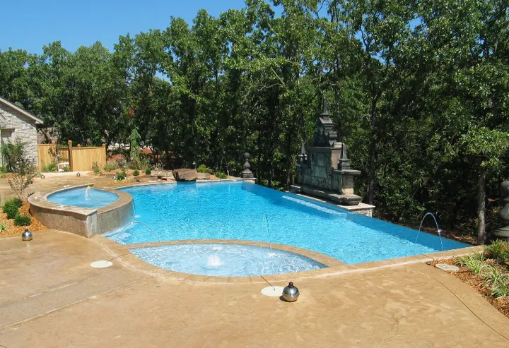Pool with attached spa, waterfall feature, and dense tree backdrop