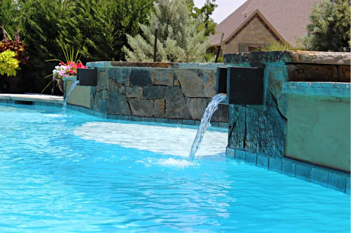 Artistic pool water feature with cascading wall and landscaping
